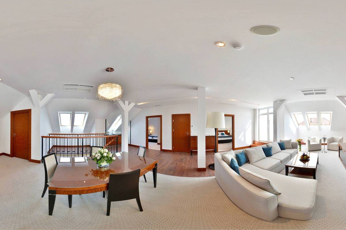 A spacious living area with a dining table, sofa, and a large TV mounted on the wall.