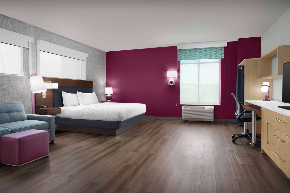 Ein modernes Hotelzimmer mit Bett, Schreibtisch, Stuhl und Fernseher.