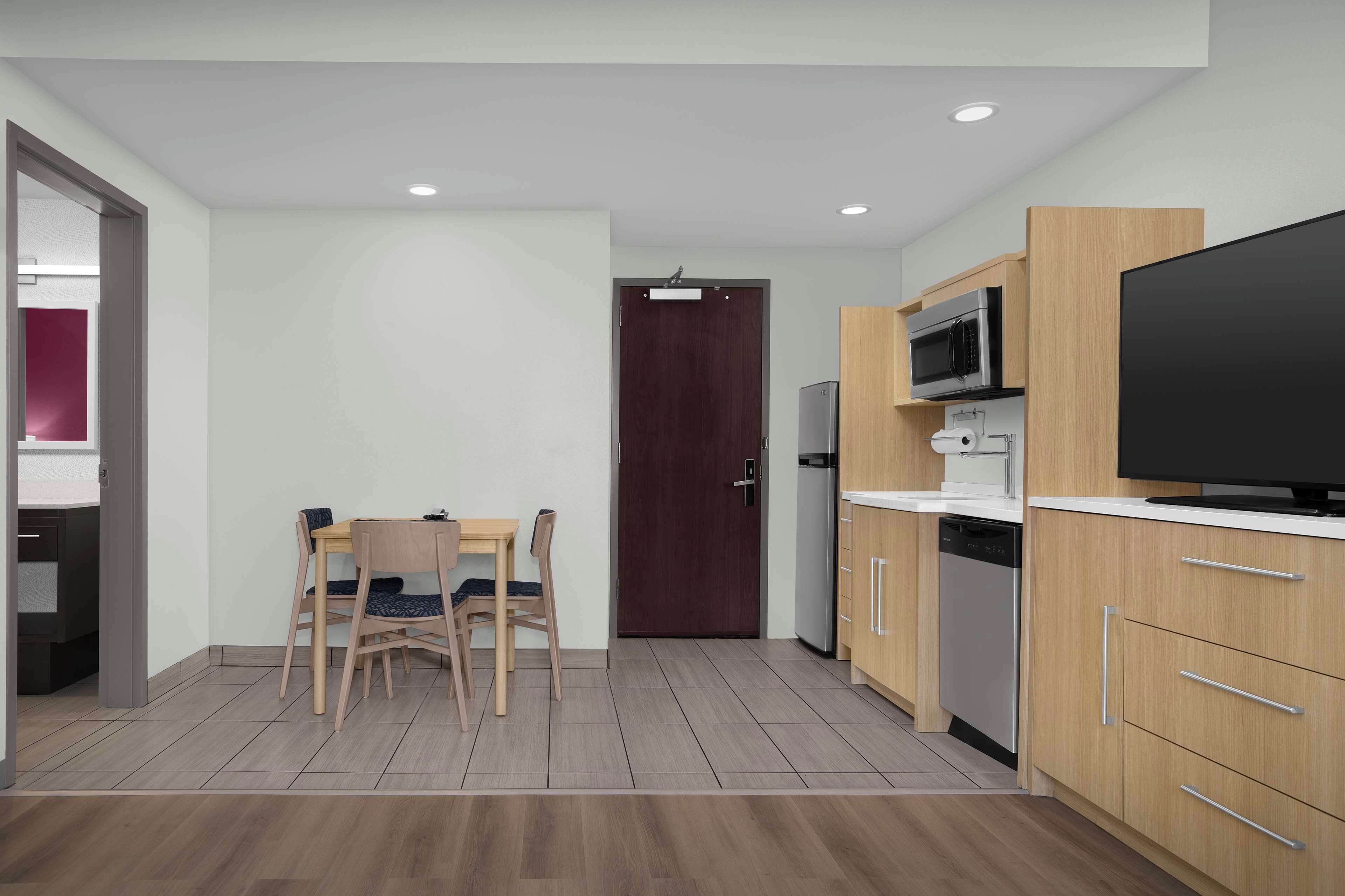 A modern kitchen with wooden cabinets, a microwave, a refrigerator, and a dishwasher. There is a dining area with a table and chairs.