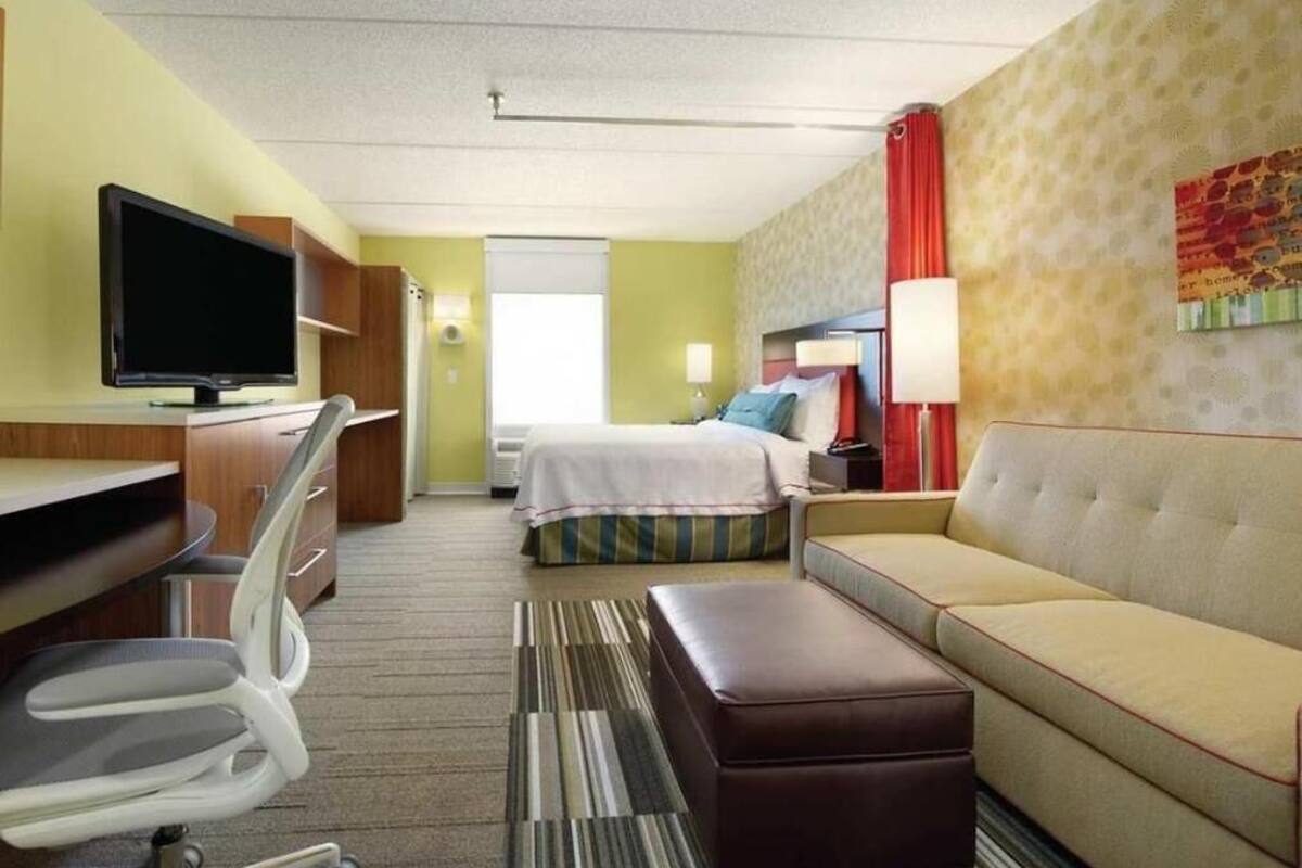 Ein Hotelzimmer mit einem Bett, einem Sofa, einem Schreibtisch mit Fernseher und einem Sessel.