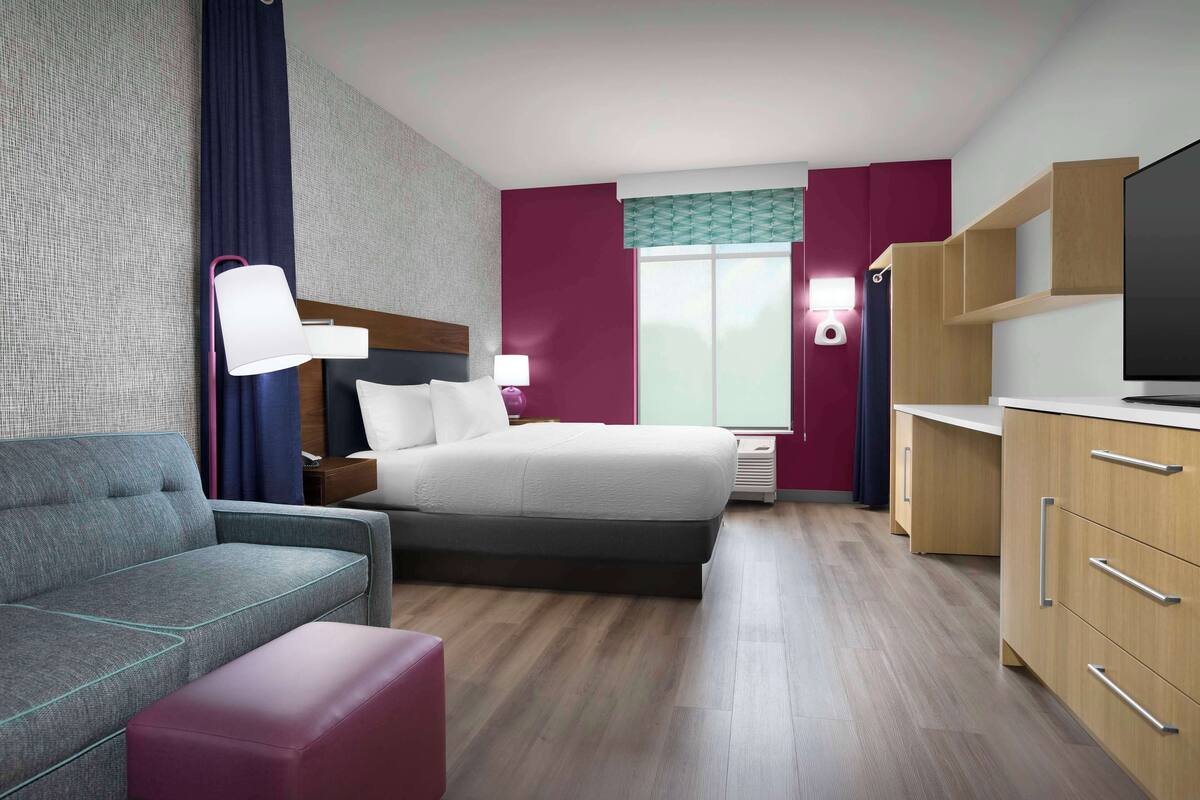 Ein Hotelzimmer mit Bett, Sofa, Schreibtisch und Fernseher.