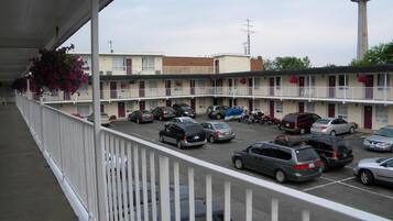 A motel parking lot with multiple cars parked, a tower in the background, and a balcony with a railing.