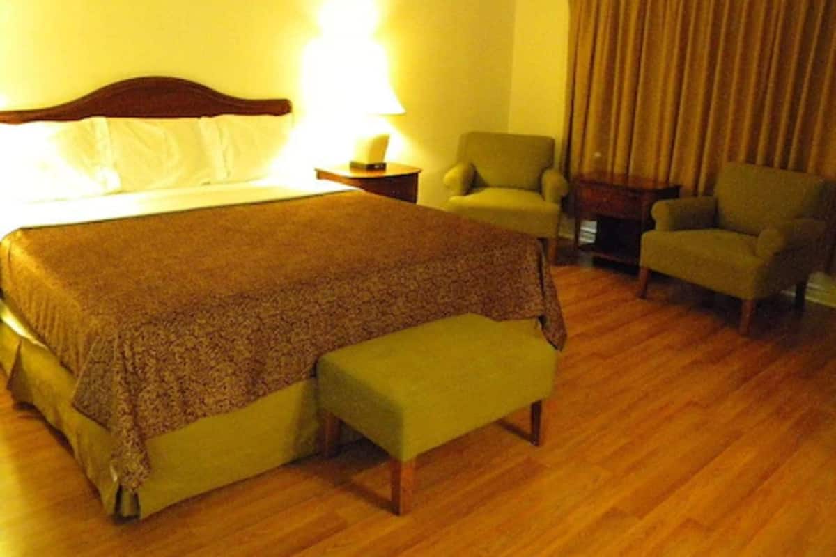 A hotel room with a large bed, a bench, two armchairs, a nightstand, and a lamp.
