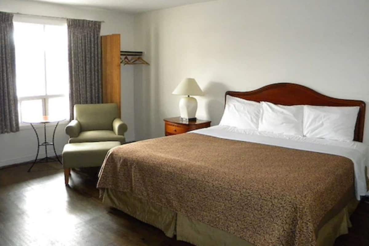 A hotel room with a large bed, a chair, a nightstand with a lamp, and a window with curtains.