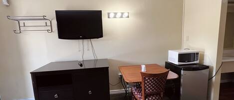 Habitación de hotel compacta con escritorio, silla, televisor y microondas.