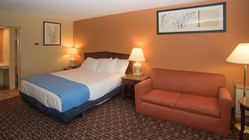 A hotel room with a bed, a sofa, two lamps, and framed artwork on the walls.