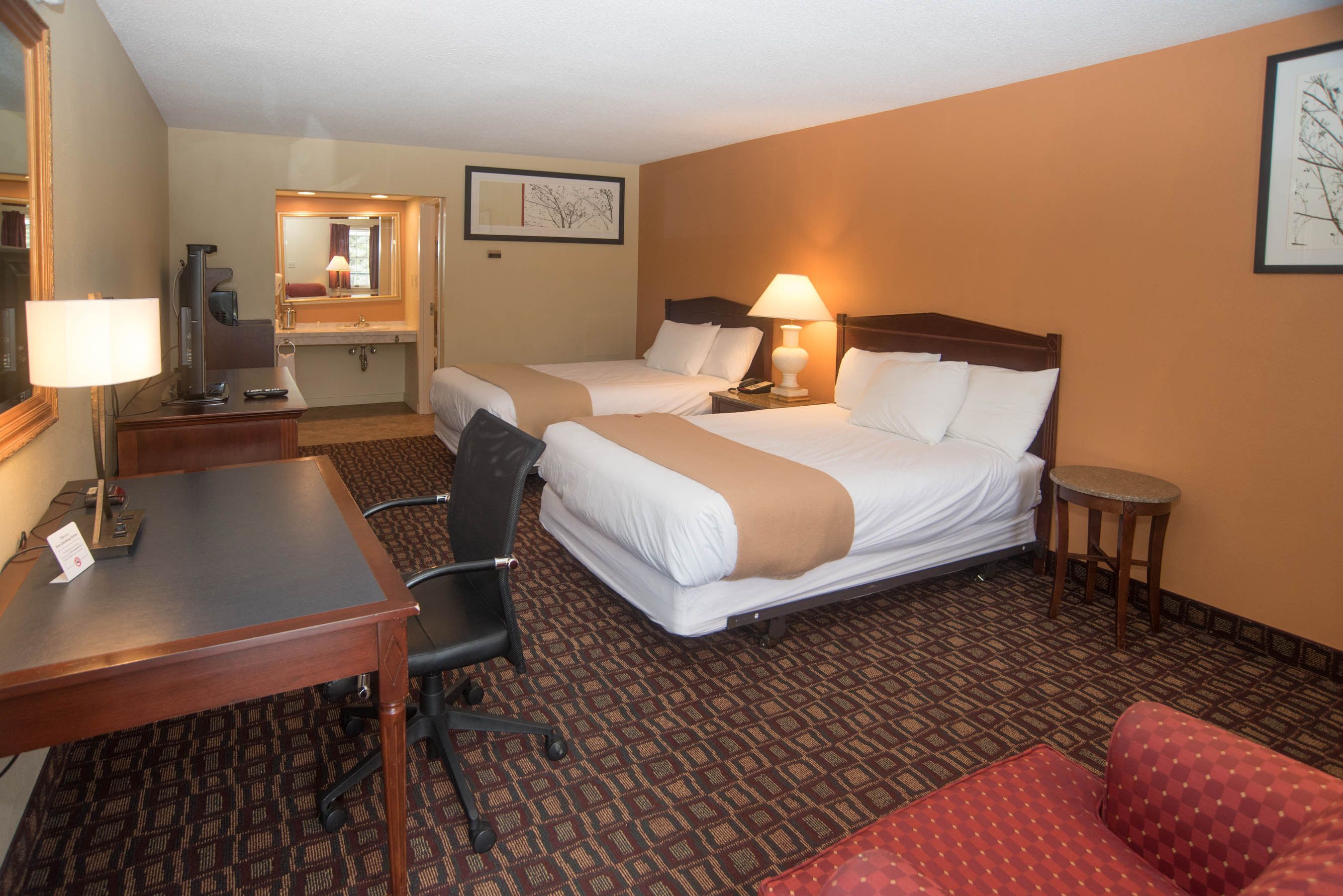 Une chambre d’hôtel avec deux lits, un bureau avec une lampe, une chaise et une petite table ronde.