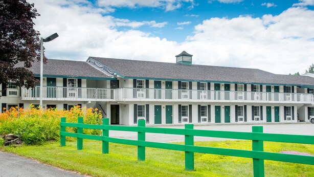A motel with a two-story structure, a covered balcony, and a green fence in front.