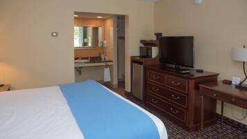 Habitación de hotel con cama, escritorio, televisor, microondas y baño visible a través de una puerta abierta.