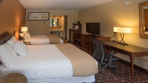 A hotel room with two beds, a desk, a television, and a desk lamp.
