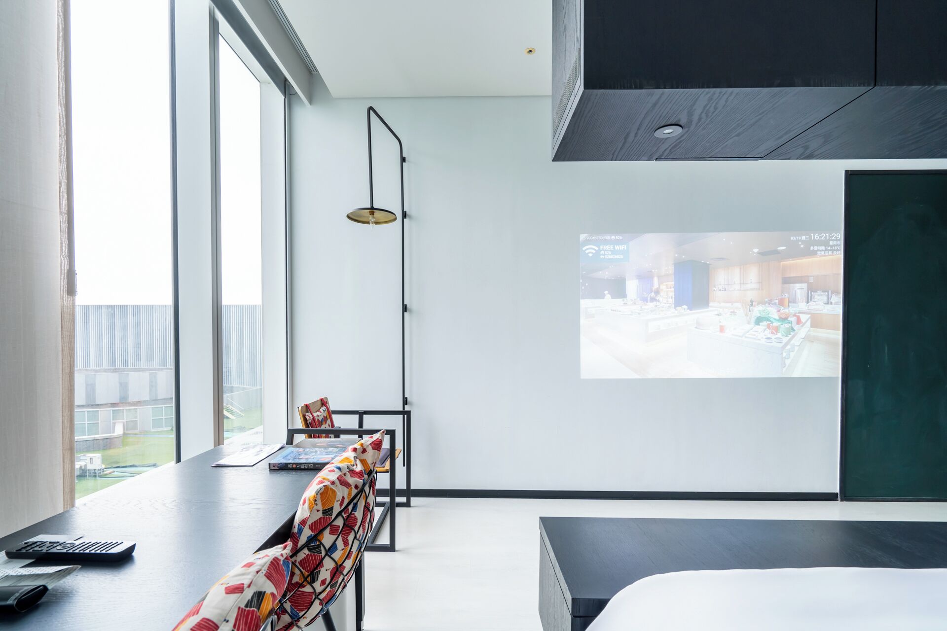 Una habitación de hotel moderna con un ventanal grande, un escritorio con una computadora portátil, una silla colorida y una cama.