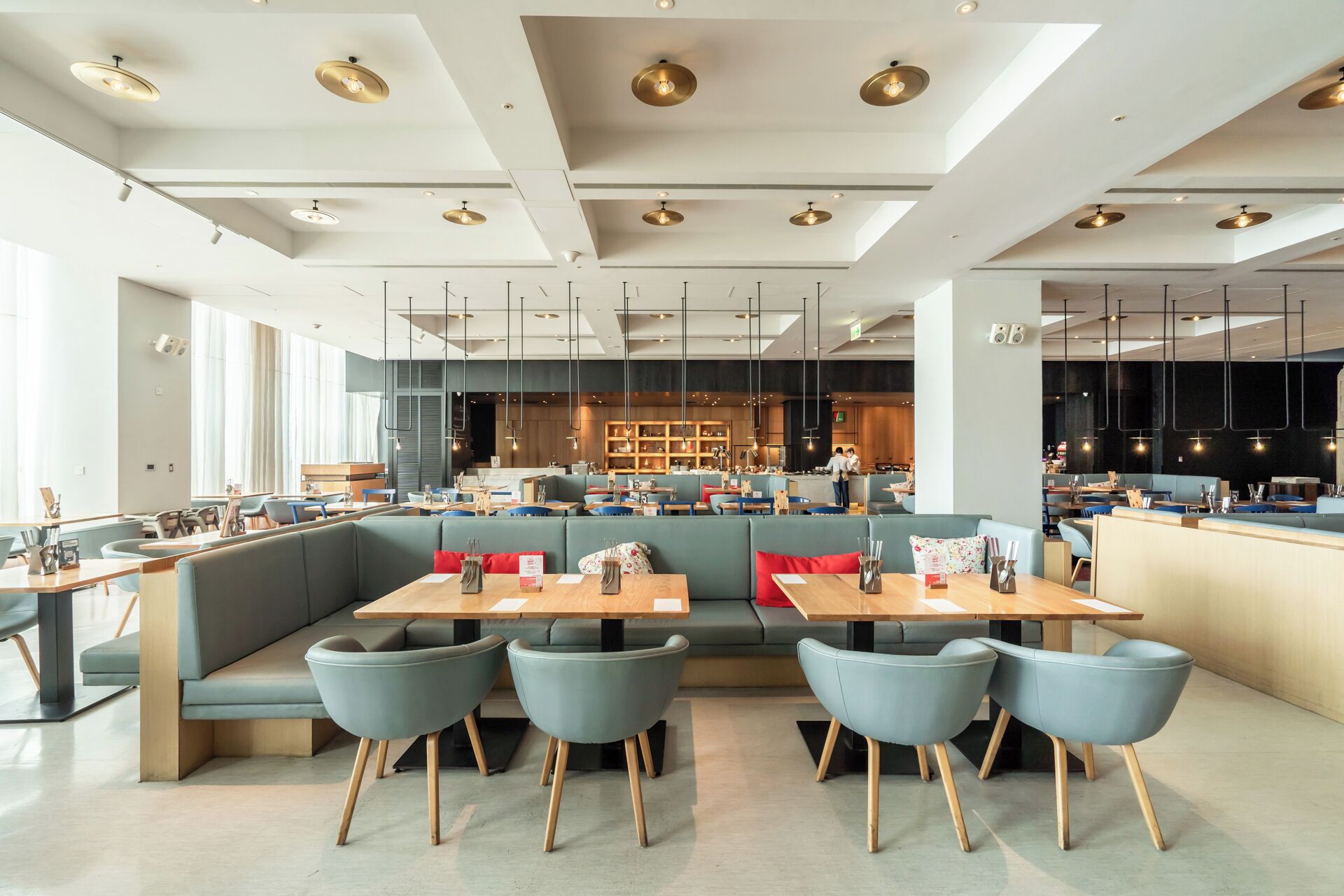 Ein modernes Restaurant-Interieur mit hohen Decken, Pendelleuchten und einer Mischung aus Sitzgelegenheiten, darunter Boxsitzgelegenheiten und Tische.
