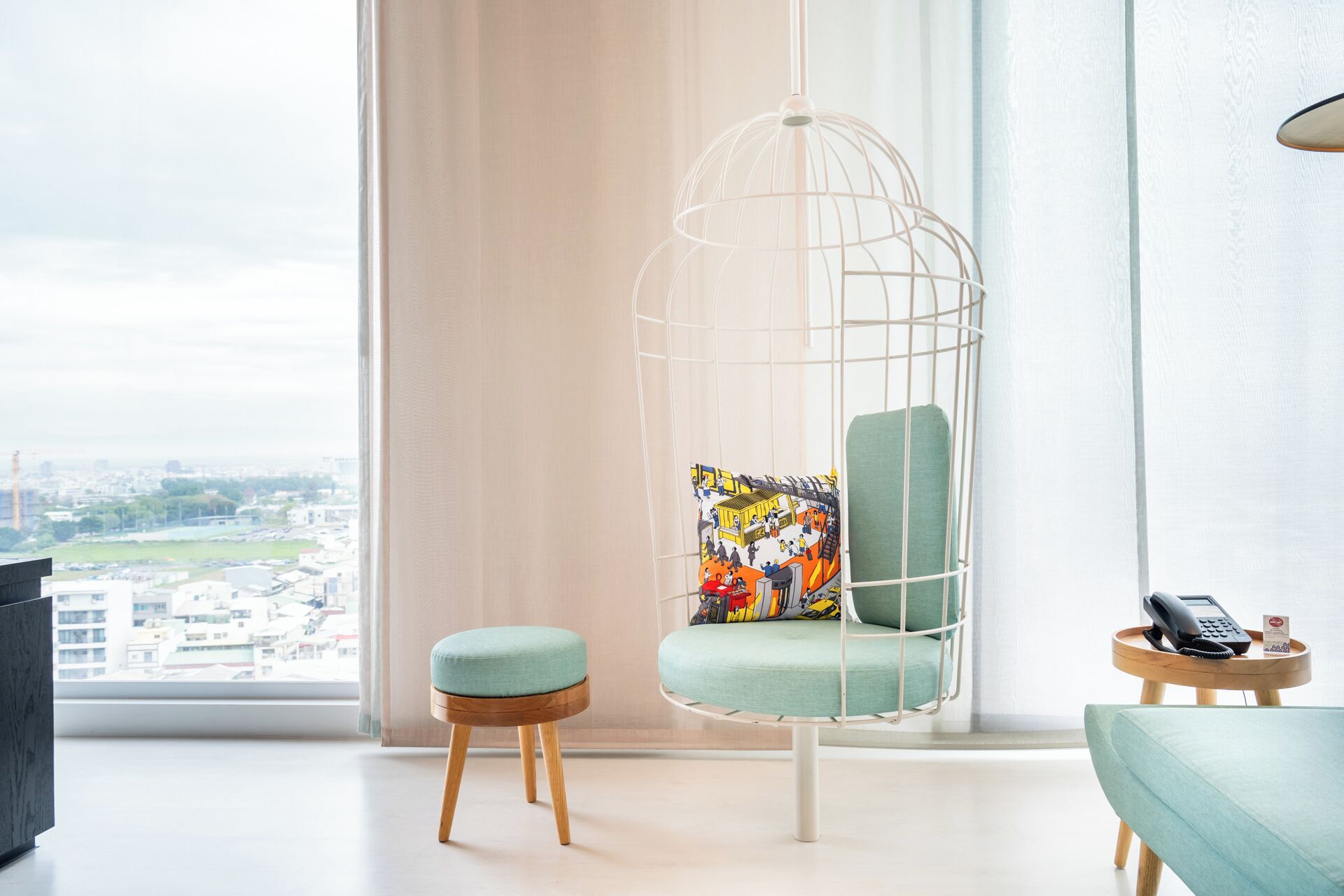 A modern room with a hanging chair, a small ottoman, and a side table with a phone and remote.