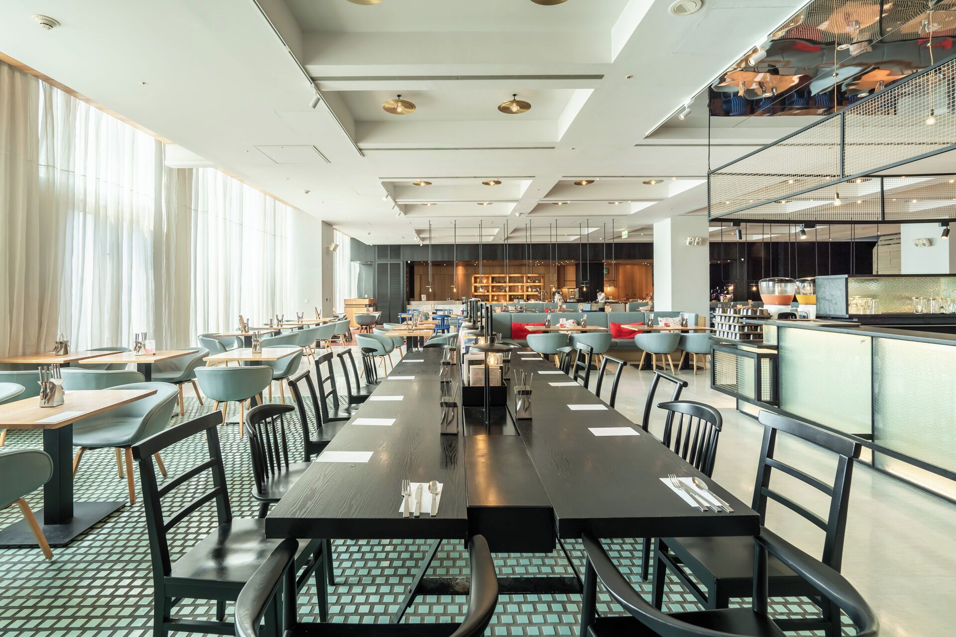 A spacious restaurant with high ceilings, modern lighting, and a mix of seating arrangements including tables and booths.