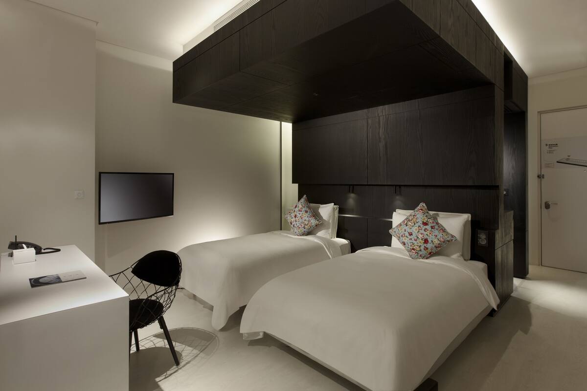 Ein modernes Hotelzimmer mit zwei Betten, einem Schreibtisch und einem Flachbildfernseher.