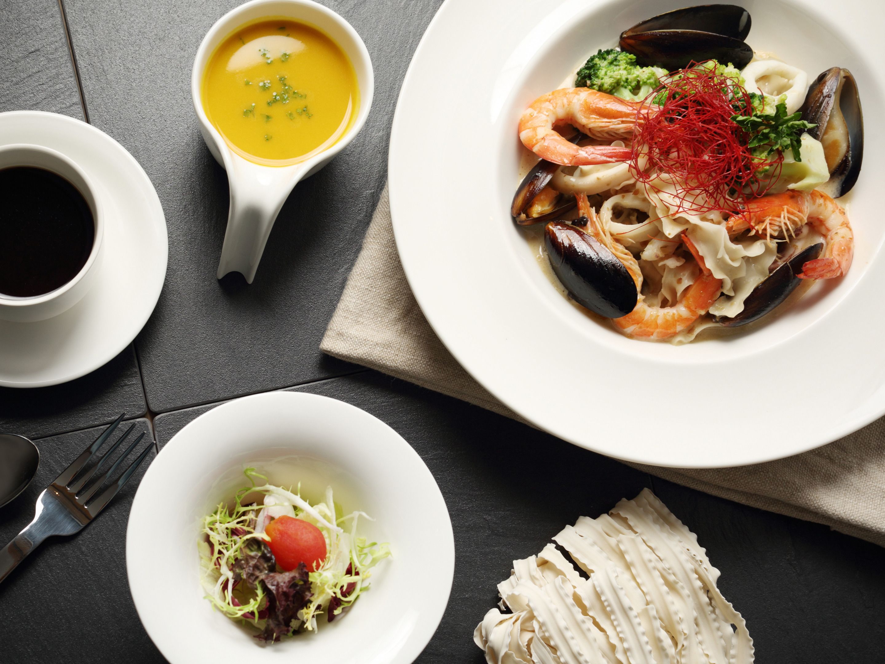 A table with a seafood dish, a bowl of soup, a salad, and a cup of coffee.