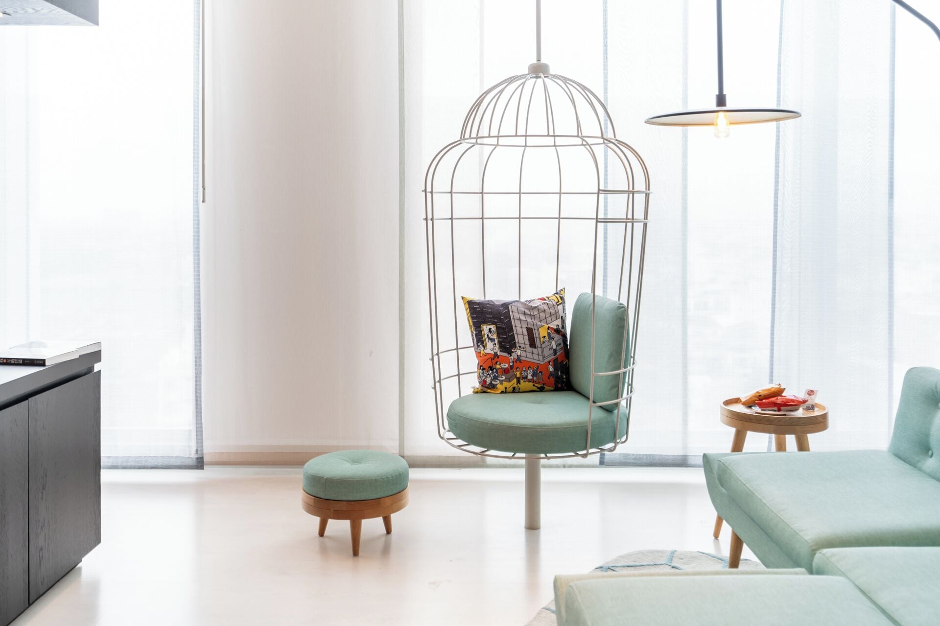 A modern living room with a hanging chair, a small ottoman, and a side table with snacks.