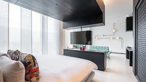 Habitación de hotel moderna con una cama grande, un escritorio, un televisor y vistas a la ciudad.
