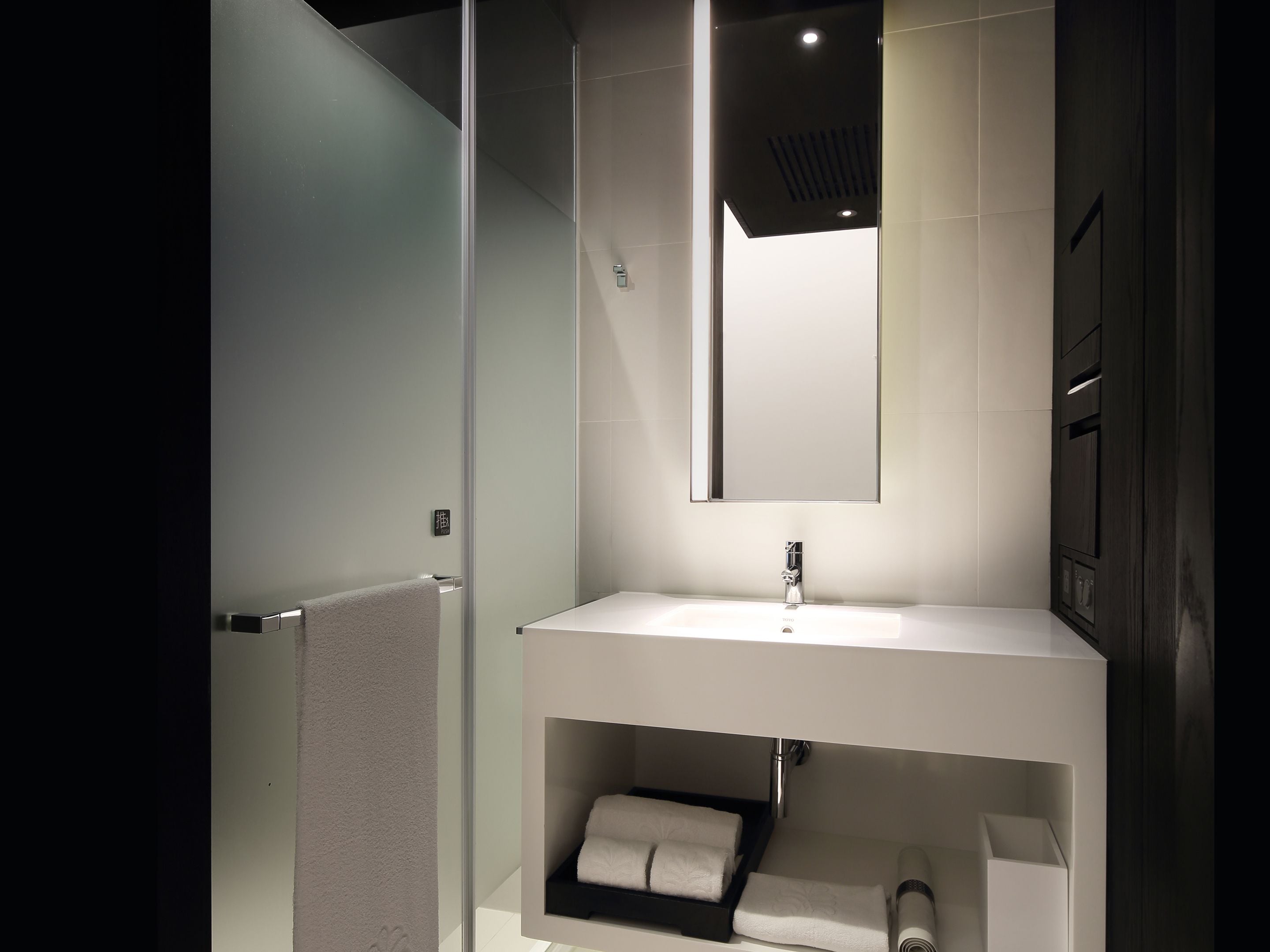 Un baño moderno con cabina de ducha de vidrio, un lavabo blanco con espejo y un perchero para toallas.
