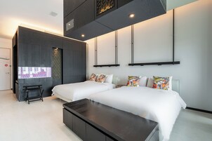 A modern hotel room with two beds, a dark wooden bench, and a large window with a decorative pattern.