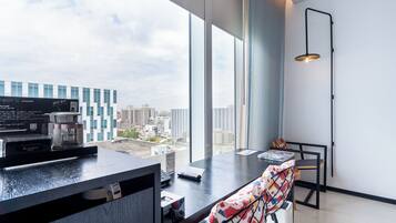 Una habitación moderna y bien iluminada con un gran ventanal que ofrece vistas a la ciudad. Hay una cafetera y una computadora portátil sobre el escritorio.