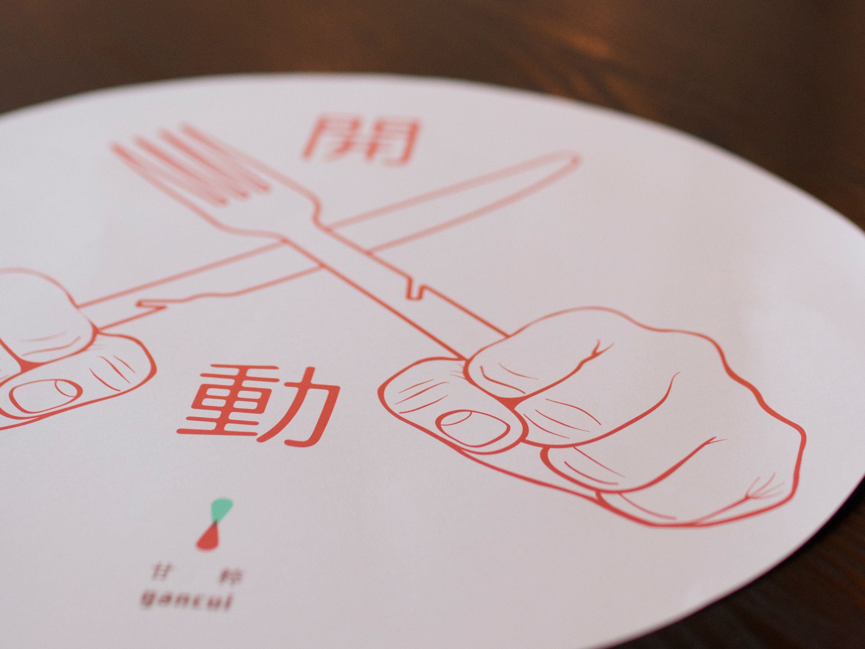 A hand holding a fork and knife crossed over each other on a white plate with red text and a small green icon.