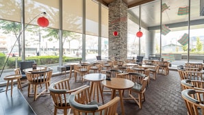 Una cafetería amplia con sillas y mesas de madera, ventanas grandes y un pilar de piedra.