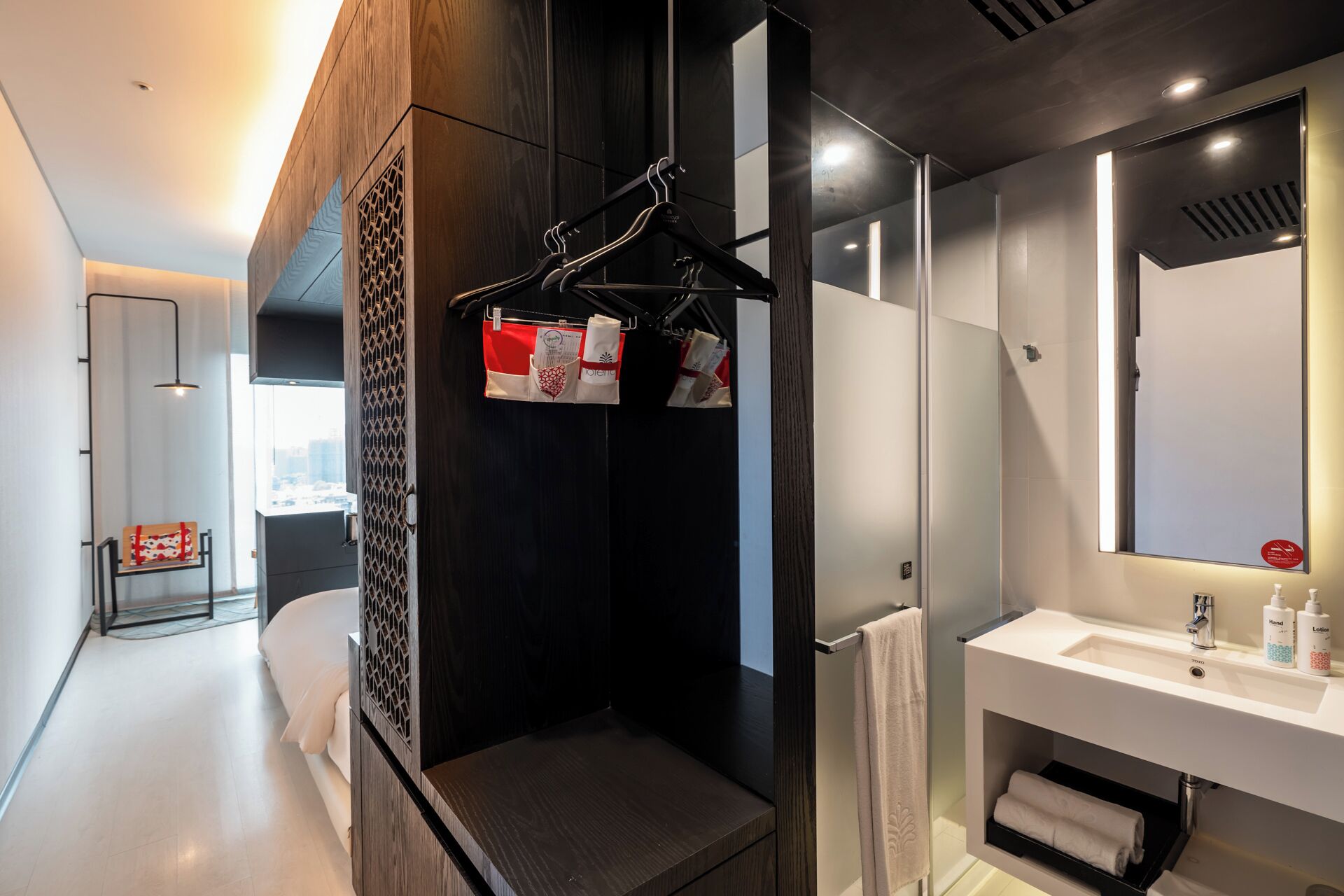 A modern bathroom with a large mirror, white sink, and a towel rack with hanging items.