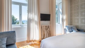 A modern hotel room with a large bed, a TV mounted on the wall, and a view of the outdoors through large windows. - Santiago de Alfama - Boutique Hotel (Lisbon)