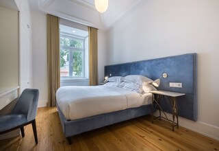 A bedroom with a bed, bedside table, chair, and a window with curtains.