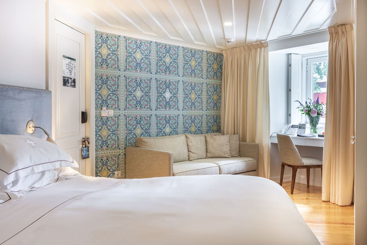 Ein Schlafzimmer mit einem Bett, einem Sofa, einem Schreibtisch und einem Fenster mit Vorhängen.