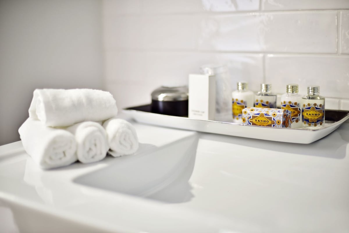 A bathroom with a white sink, a towel rack with rolled towels, and a tray with toiletry bottles.