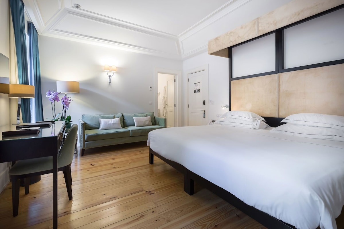 Une chambre d’hôtel équipée d’un lit, d’un bureau, d’une chaise, d’un canapé et d’une lampe fixée au mur.