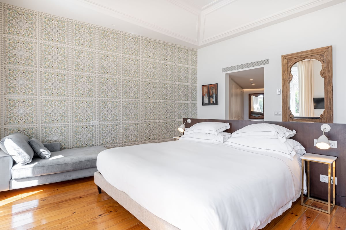 Ein Schlafzimmer mit einem großen Bett, einer grauen Couch, strukturierter Tapete und Holzboden.
