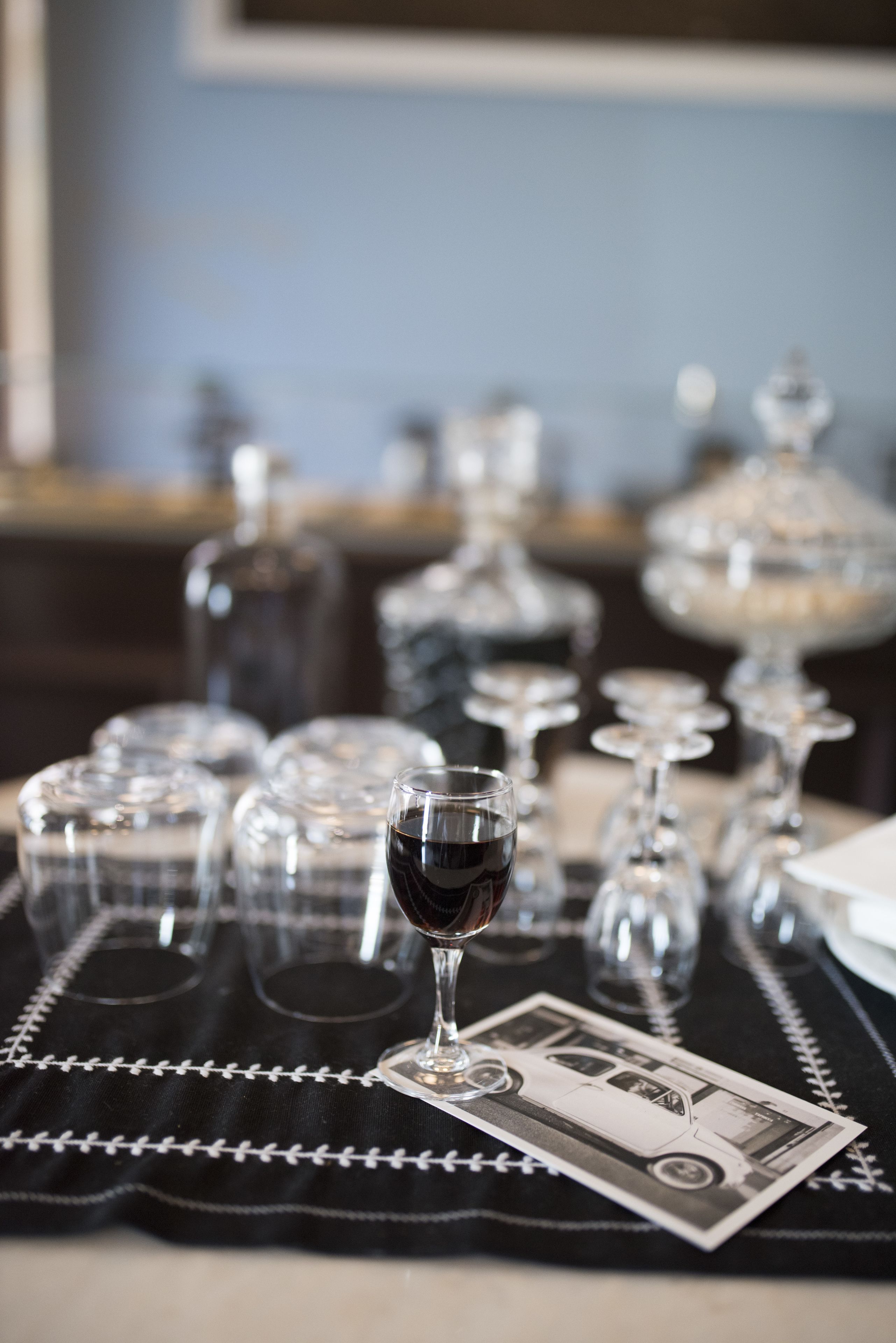 Una mesa con copas de vino y botellas, un posavasos con forma de coche y un billete de dólar.