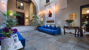 A lobby with a blue sofa, potted plants, a reception desk, and a stone floor. - Santiago de Alfama - Boutique Hotel (Lisbon)
