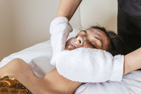 A person lying on a bed with a white towel draped over their head.