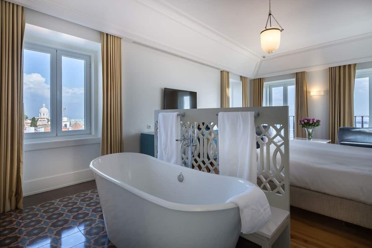 Ein modernes Hotelzimmer mit Badewanne, einem Bett, einem Fernseher und Blick auf die Stadt.