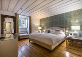 A bedroom with a large bed, a glass desk, and a patterned wall.