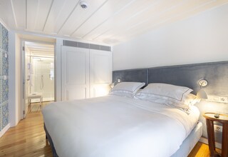 A bedroom with a large bed, a bedside table with a lamp, and a shower area visible through an open door.