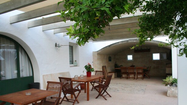 Une terrasse extérieure avec des tables et des chaises en bois, une plante en pot et un mur de pierre en arrière-plan.