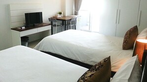 A hotel room with two beds, a desk with a TV, a small table, and a window with curtains. - Wealth 30th Apartment (Bangkok)