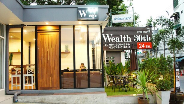 A modern cafe with a wooden facade, large windows, and outdoor seating. - Wealth 30th Apartment (Bangkok)