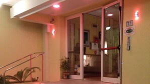 A set of outdoor stairs leading to a building entrance with glass doors and a potted plant at the bottom. - Hotel Angela (Misano Adriatico)