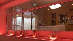 A reception area with a red-lit reception desk, a mirror reflecting the interior, and a door leading to another room. - Hotel Angela (Misano Adriatico)