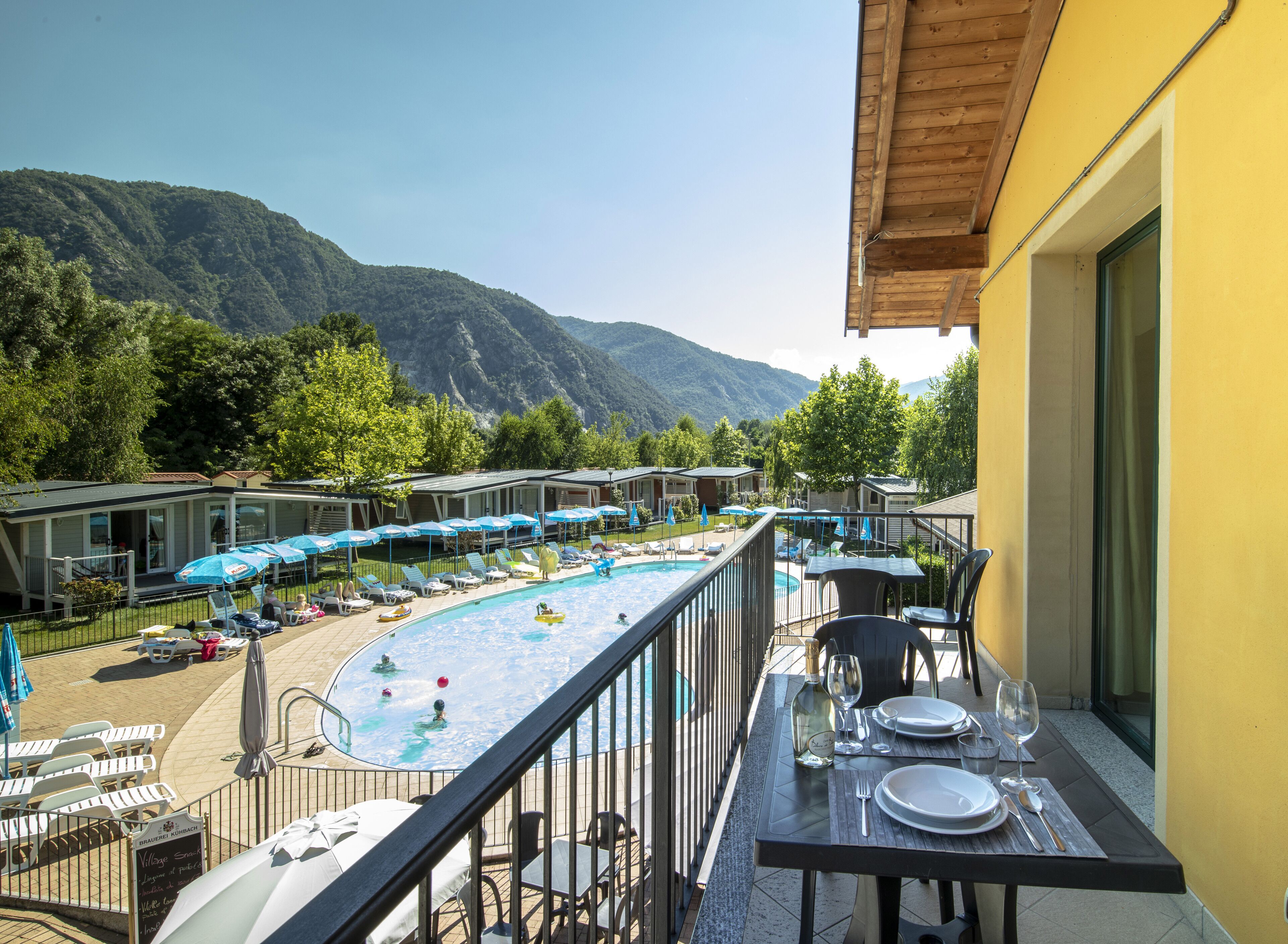 A pool area with lounge chairs and umbrellas, a dining table set with plates and glasses, and a mountain view in the background.