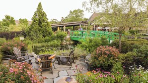 Un patio aménagé en jardin, avec un sol en pierre, des chaises en bois, un foyer et un bassin.