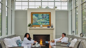Un espace de détente intérieur, chaleureux, avec des meubles en osier, une cheminée et un grand tableau accroché au-dessus.