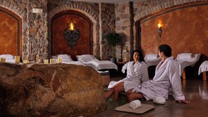 Une salle de spa aux murs en pierre, avec une grande roche servant d’élément central et plusieurs lits dotés de draps blancs.