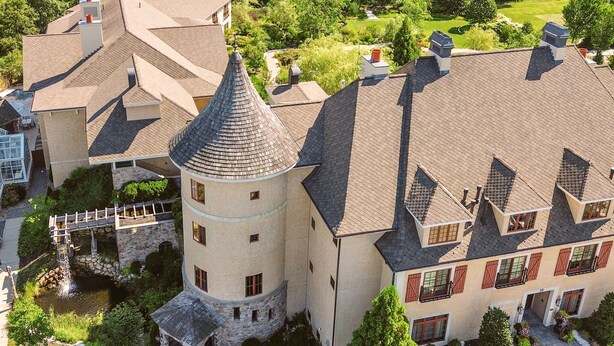 Un grand bâtiment historique doté d’une tour imposante, d’une cour intérieure agrémentée d’un petit élément décoratif aquatique et d’un jardin bien entretenu.